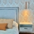 Respaldo de cama con tachas en un dormitorio moderno, con almohadas decorativas y una lámpara de pared encendida.