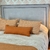Respaldo de cama en tonos grises con almohadas de colores cálidos sobre un edredón claro.
