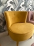 Poltrona Nantes de color amarillo, con un diseño moderno y botones decorativos, situada en un ambiente con fondo de hojas verdes.