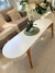 Mesa ovalada baja de color blanco con patas de madera, decorada con una planta en una maceta blanca y un mantel verde, ubicada en un ambiente moderno.