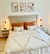 Acolchado Queen con almohadas decorativas en una cama moderna, con paredes blancas y cuadros artísticos en la parte superior.