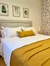 Cubrecama King Size en una cama con almohadas blancas y un cojín amarillo, en un ambiente decorado con cuadros y una pared con diseño floral.