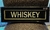 Cartel antiguo decorativo que dice "WHISKEY" en letras grandes y blancas sobre un fondo negro.