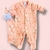 Macacão para bebê menina na cor salmão com estampa de folhas, detalhes de corações e botões de pressão na frente, acompanhado de naninha em formato de gatinha azul com detalhes de sorriso e orelhas, ideal para maternidade.