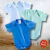 Kit com três bodies lisos para bebê nas cores azul royal, verde e azul claro, exibidos sobre superfície de madeira e tapete branco