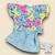 Conjunto de roupa para bebê menina com blusa floral colorida e saia azul clara.