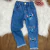 Calça jeans infantil para menina com estampa do personagem Stitch, detalhes em azul e rosa, com barra desfiada.