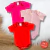 Kit com três bodies lisos para bebê nas cores rosa bebê, vermelho e pink, com manga curta, dispostos sobre superfície branca e madeira.