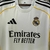 Camisa Home do Real Madrid 25/26, predominantemente branca, com detalhes em amarelo e logo da Adidas.