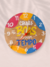 Placa redonda de MDF com 20cm pendurada na parede com um lettering, escrito em branco: Coisas boas levam tempo, com gancho na máquina do relógio para pendurar na parede da casa