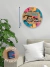 Placa redonda de MDF com 20cm pendurada na parede com um lettering, escrito em preto: Nesta casa felicidade não tem hora, com gancho na máquina do relógio para pendurar na parede da casa
