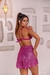 Modelo usando uma saia curta pink com brilho, vista de costas, em ambiente com paredes claras e luminárias.