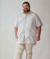 Homem sorridente vestindo uma camisa de viscolinho cinza claro, com botões e mangas curtas,plus size, em um fundo neutro.