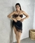 Mulher usando uma saia de franjas preta, com um top marrom, em um ambiente neutro.