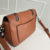 Bolsa pequena de couro marrom com duas alças e detalhes em corrente prateada.