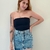 Modelo usando um tube top preto com uma saia jeans, destacando o estilo casual e moderno da peça.