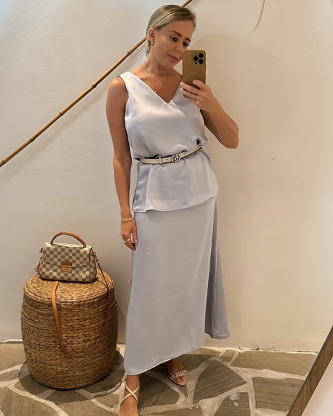 Mulher vestindo uma saia longa Julia em um ambiente iluminado, posando para a foto com uma bolsa e sandálias.