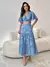 Modelo está usando o tamanho P do conjunto bordado em azul, composto por blusa com mangas amplas e saia longa com detalhes florais bordado.