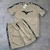 Conjunto masculino da Mizuno composto por camiseta e short na cor bege, com logotipo em preto e detalhes em preto nas laterais.