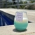 Vela de cera de coco com aroma de verão, posicionada ao lado de uma piscina.