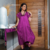 Modelo usando um vestido roxo com capuz e bolsos, posando em um ambiente moderno.
