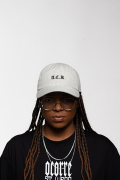 Modelo usando um boné Dad Hat A.C.R no Off White, com camisa preta da marca OCORRE.