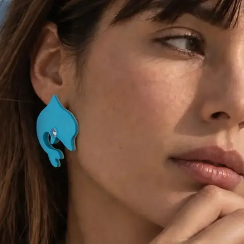 Arete maxi azul con diseño de delfín usado en la oreja de una mujer