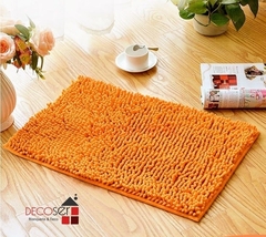 Alfombra de baño shaggy de color naranja con base antideslizante, presentada sobre un piso de madera.