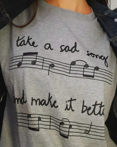 camiseta cinza com desenho de uma partitura e notas musicais com carinhas, e a frase "take a sad song and make it better", em tamanho adulto, sem gênero