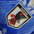 Emblema da seleção japonesa de futebol, destacando o símbolo do Japão e o nome JFA em um fundo de camisa azul.