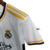Kit infantil do Real Madrid para a temporada 2023/24, composto por camisa branca com detalhes em amarelo e shorts.