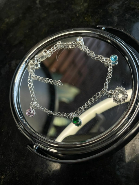 Pulseira de prata 925 com berloques em forma de coração e zircônias coloridas, apresentada em uma superfície espelhada.