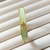 Bracelete dourado com cruz cravejada e resina verde, usado no pulso.