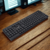 Teclado inalámbrico dual Bluetooth 5.0 y 2.4GHz sobre una mesa de madera.