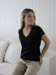 Modelo luciendo una remera negra con escote en V, combinada con pantalones claros, en un ambiente luminoso y relajado.