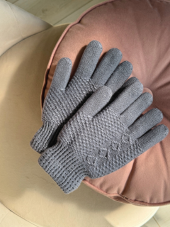 Guantes de lana grises sobre un cojín rosa, con detalles texturizados y diseño de cinco dedos.
