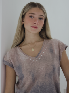 Modelo luciendo una remera de color tierra con detalles en el escote y fondo claro.