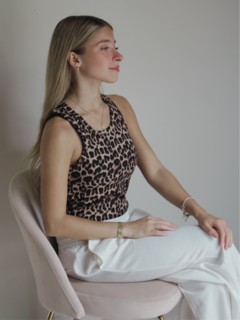 Mujer sentada en una silla, vistiendo una musculosa de estampado animal, con cabello largo y lacio, en un entorno minimalista.