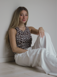 Modelo sentada con musculosa de estampado de leopardo y pantalones blancos en un ambiente minimalista.