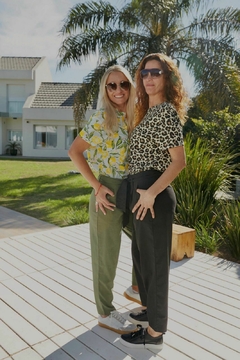 Dos mujeres posando en un entorno al aire libre, vistiendo remeras de estampados coloridos y pantalones elegantes.