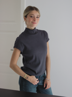 Modelo luciendo una polera sombra de cuello alto, en un entorno minimalista.