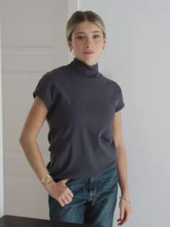 Modelo vistiendo una polera sombra de color gris oscuro con cuello alto y mangas cortas, en un entorno luminoso.