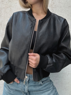 Campera de cuero negra con cierre, estilo bomber, llevada por una mujer con jeans claros.