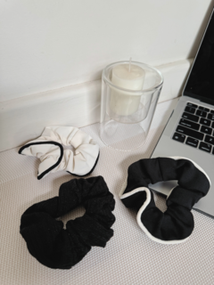 Scrunchies para el pelo en colores blanco y negro, junto a una vela y una laptop.