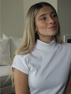 Modelo usando una polera blanca de manga corta con cuello alto, en un ambiente interior.