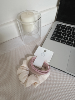 Dos scrunchies para el pelo, uno en color crema y otro en color rosa, sobre una superficie texturizada junto a una vela y una laptop.