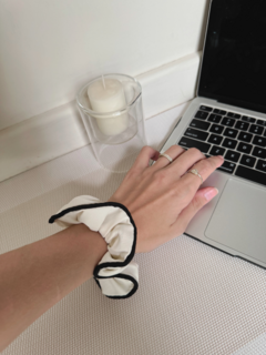 Scrunchie blanco con borde negro en la muñeca de una persona, junto a una laptop y una vela encendida.
