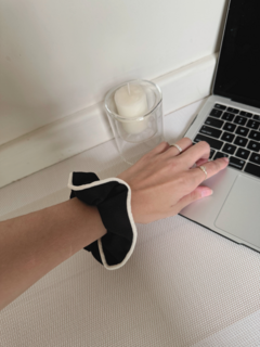 Una mano con una scrunchie negra con borde blanco sobre la muñeca, junto a una laptop y una vela encendida.