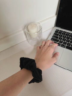 Scrunchie negro en la muñeca de una persona, junto a una laptop y una vela encendida.