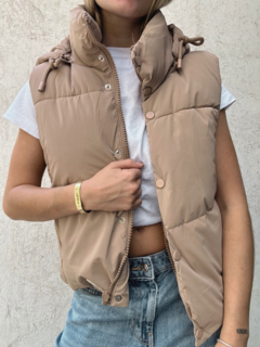 Chaleco Huracán en color beige, con cuello alto y cierre frontal, usado por una modelo con camiseta blanca y jeans cortos.